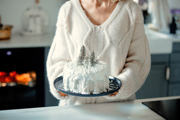 Woman holding christmas cake with cream on table at kitchen