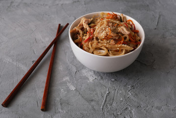 Fried udon noodles with chicken meat and sesame in white bowl on a gray concrete background