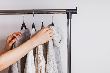 Woman choosing one of the warm cozy knitted sweaters sweaters on hangers.