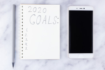 2020 new year goals, plan, action text on notepad on white marble background. 2020 goals on blank note paper with copy space for text and smartphone. Cup of coffee over marble background