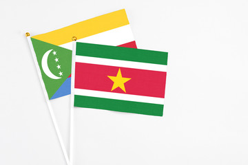 Suriname and Comoros stick flags on white background. High quality fabric, miniature national flag. Peaceful global concept.White floor for copy space.