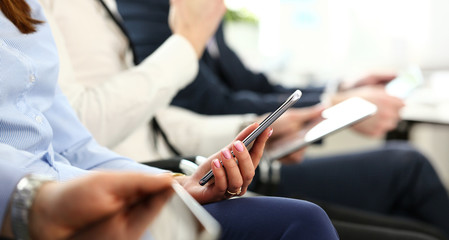 Bunch of people holding in hands electronic gadgets while sitting in line