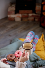 girl with a cup of coffee and donuts by the fireplace at home