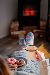 girl with a cup of coffee and donuts by the fireplace at home