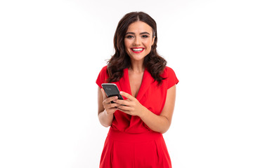 A young woman with bright makeup, in a red summer dress stands with a phone in hand and smiles