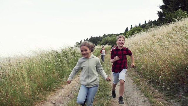 Front view of group of school children running on field trip in nature.