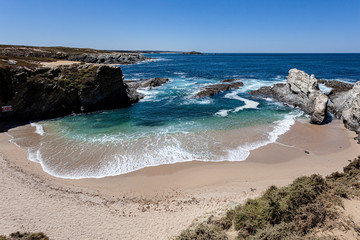 Pequena praia de água cristalina protegida das ondas do oceano pelas rochas.