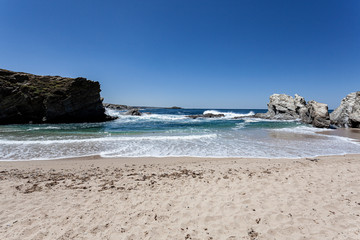 Fototapeta na wymiar Ondas numa praia tranquila protegida das ondas do oceano pelas rochas.