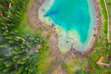 Aerial view of turquoise blue water of lake Carezza in Alps Dolomites. Lago di Karersee near fir tree forest.