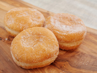 Three fresh tasty doughnuts with sugar coating on a wooden board. Close up.