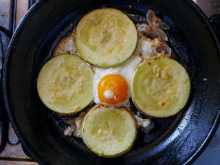 Cooking fresh vegetable marrow on a frying pan with egg. Close up.