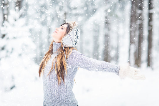 Young, beautiful woman with winter cap and gray sweater and closed eyes in winter landscape