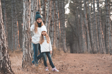 Girls 5 and 10 years old wearing knitted casual clothes posing in forest over nature background. Looking at camera. Winter season. Childhood.