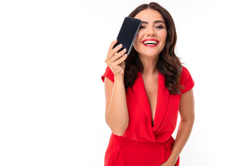 A young woman with bright makeup, in a red summer dress stands with a phone in hand and smiles