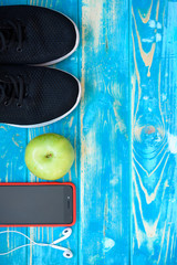 Sneakers, earphones and drinking water on blue background. Sport equipment.