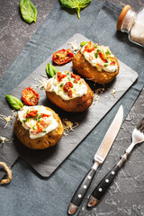 Baked stuffed potatoes with bacon, tomato and cheese on stone background.
