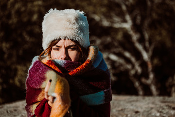 .Pretty young woman enjoying a sunny winter day outdoors. Surrounded by nature, relaxed and carefree. Covering from the cold with a burgundy scarf and wearing a fur hat. Lifestyle