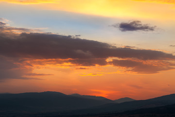 Amazing light on the cloud formations beautifully colored by sunset light and silhouettes of distant horizon mountains