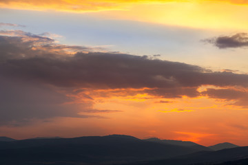 Amazing light on the cloud formations beautifully colored by sunset light and silhouettes of distant horizon mountains