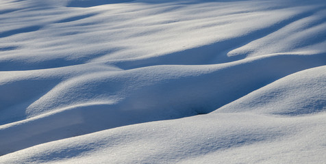 Abstract shapes in snow created by wind. Ice cold snow texture with long shadows, snow dunes.