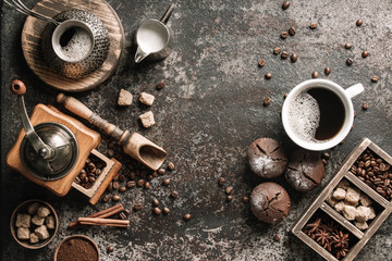Coffee cup with coffee grinder and coffee beans on dark textured background.