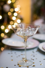 Celebratory champagne glass surrounded by Christmas decorations and holiday moods. Luminous garlands, golden sweets and a festive table set with a Christmas tree.