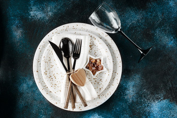Festive table place setting. Crockery and cutlery on a dark textured background with copy space. Christmas Xmas New Year holiday