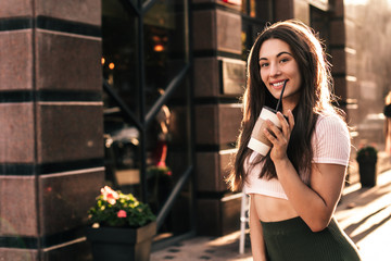 Beautiful smiling woman drink coffee walking on the city in summer day.
