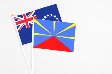 Fototapeta premium Reunion and Cook Islands stick flags on white background. High quality fabric, miniature national flag. Peaceful global concept.White floor for copy space.
