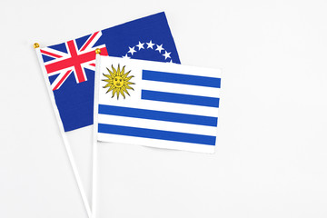 Uruguay and Cook Islands stick flags on white background. High quality fabric, miniature national flag. Peaceful global concept.White floor for copy space.