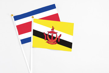 Brunei and Costa Rica stick flags on white background. High quality fabric, miniature national flag. Peaceful global concept.White floor for copy space.