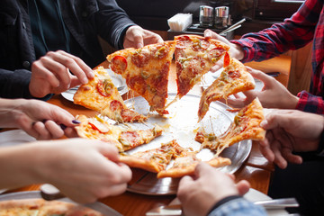 group of students friends eat Italian pizza, hands take slices of pizza in a restaurant