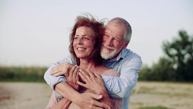 Affectionale senior couple on a holiday standing by the lake, hugging. Slow motion.