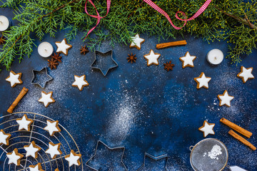 Christmas baking composition with cookies, cookies cutters, flour, spices and green fir branches on blue vintage background, top view, copy space. Winter holiday time concept
