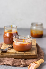 Homemade salted caramel sauce in glass jars on wooden cutting board. Selective focus.