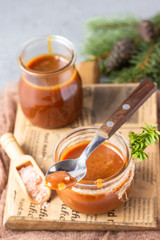 Spoon with tasty caramel sauce over glass jar as a gift for Christmas or New year with fir branches and cones. Selective focus.