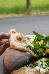 Female hand take a piece of Fresh italian pizza with tomatoes, cheese, basil on green grass background. Copy space. Homemade with love. Fast delivery. Recipe and menu