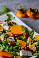 Salad with persimmon, rucola, mandarins, gorgonzola cheese, cranberry, walnuts and pine nuts. Autumn healthy salad
