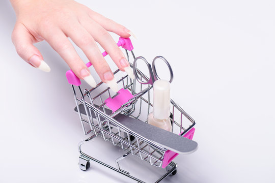 Nail polish, scissors, nail file, shopping cart with cosmetics. Online cosmetics store for women. Shopping cart with makeup for nails. Hand girl with beautiful nails. Manicure set for nail care.