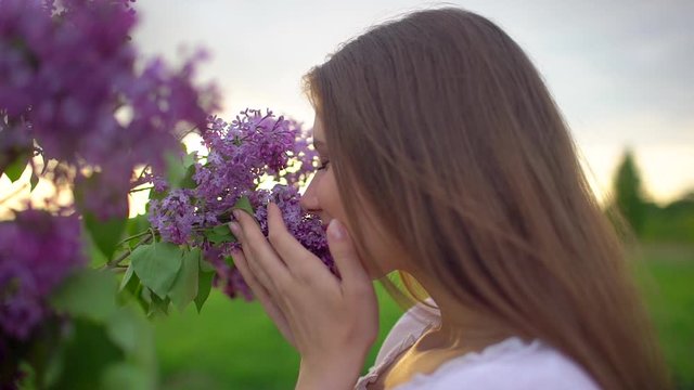 Young romantic smiling beautiful woman girl sniffing smelling lilac flowers in bouquet in nature outdoors, Inhaling aroma of flowers enjoying smell fragrance perfume freshness spring summer Beauty