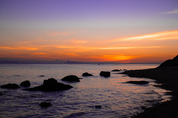 Fototapeta na wymiar Amazing colorful sunset in orange and liliac at rocky beach in south of Thailand.