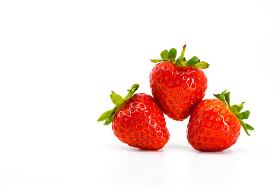 Close up of three ripe strawberries balancing on each other. All are isloated against a plain white background with space for copy on the right.