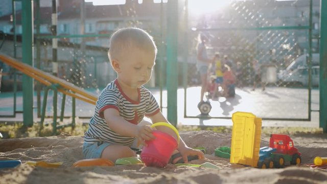 Little boy playing with toys in the sandbox at sunset.