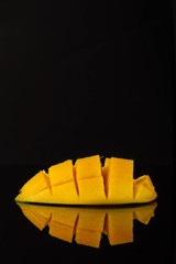 Ripe yellow mango slice on a mirror black table. Mango with reflection.