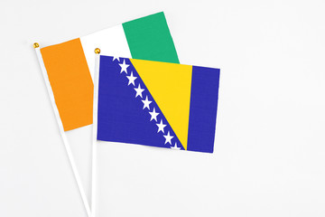 Bosnia Herzegovina and Cote D'Ivoire stick flags on white background. High quality fabric, miniature national flag. Peaceful global concept.White floor for copy space.