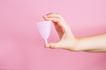 Close up of a young woman hands holding reusable pink silicone menstrual cup on pink background