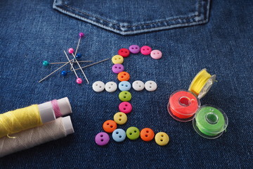 Fototapeta na wymiar Sewing and repair of clothes. The pound sign is laid out on buttons on jeans. Thimble, needle, thread, pins