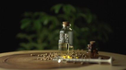 Obraz premium Very close view of CBD oil, oral syringe, pills for anxiety and stress relief near the glass jar on the wood circle tree ring table with ripple line pattern. Revolution in pain treatment and healing.