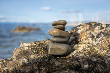 Fototapeta na wymiar Five stones cairn tower, rock zen sculpture, brown beige pebbles on the rock and sea light blue background