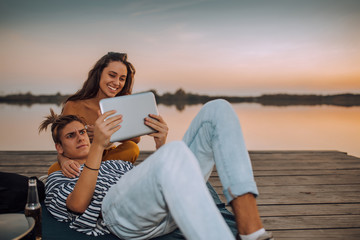 Young couple watching videos or sharing media content from a tablet, while sitting by the river